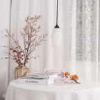 Clérachic Black and White Alabaster Pendant Light unlit over a lace table with books, blossom stems, and sheer curtains.