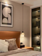 Clérachic Black and White Alabaster Pendant Light hangs low over a wood nightstand in a bedroom with framed abstract art.
