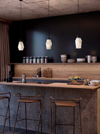 Three Clérachic Black and White Alabaster Pendant Lights glow over a wood kitchen island with brown stools and a dark shelf.