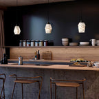 Three Clérachic Black and White Alabaster Pendant Lights hang over a thick wood bar, jars lining the black kitchen wall.