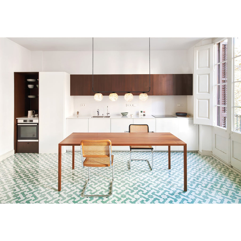 Clérachic four-globe pendant lighting a walnut dining table in a white kitchen with patterned green floor tiles.