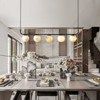 The Clérachic five-globe bar warming a set dining table, its light landing evenly along the length of the setting.