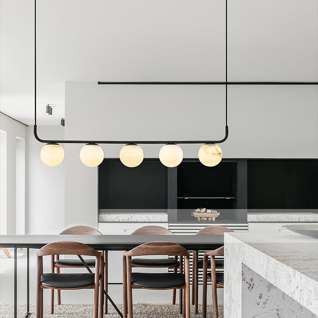 Clérachic bar pendant over a dining table in a pale minimalist kitchen, five alabaster globes glowing beside walnut chairs.