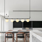 Clérachic bar pendant over a dining table in a pale minimalist kitchen, five alabaster globes glowing beside walnut chairs.