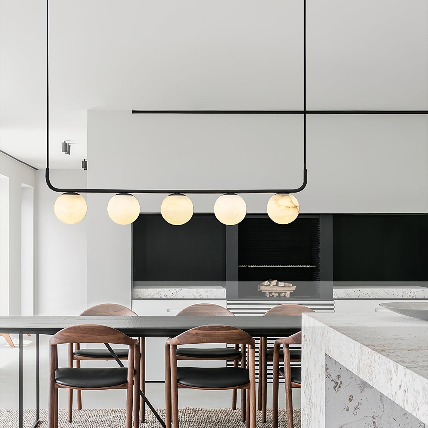 Clérachic bar pendant over a dining table in a pale minimalist kitchen, five alabaster globes glowing beside walnut chairs.