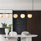 Five lit globes of the Clérachic pendant against a chalkboard wall and fluted dark timber, above an oval dining table.