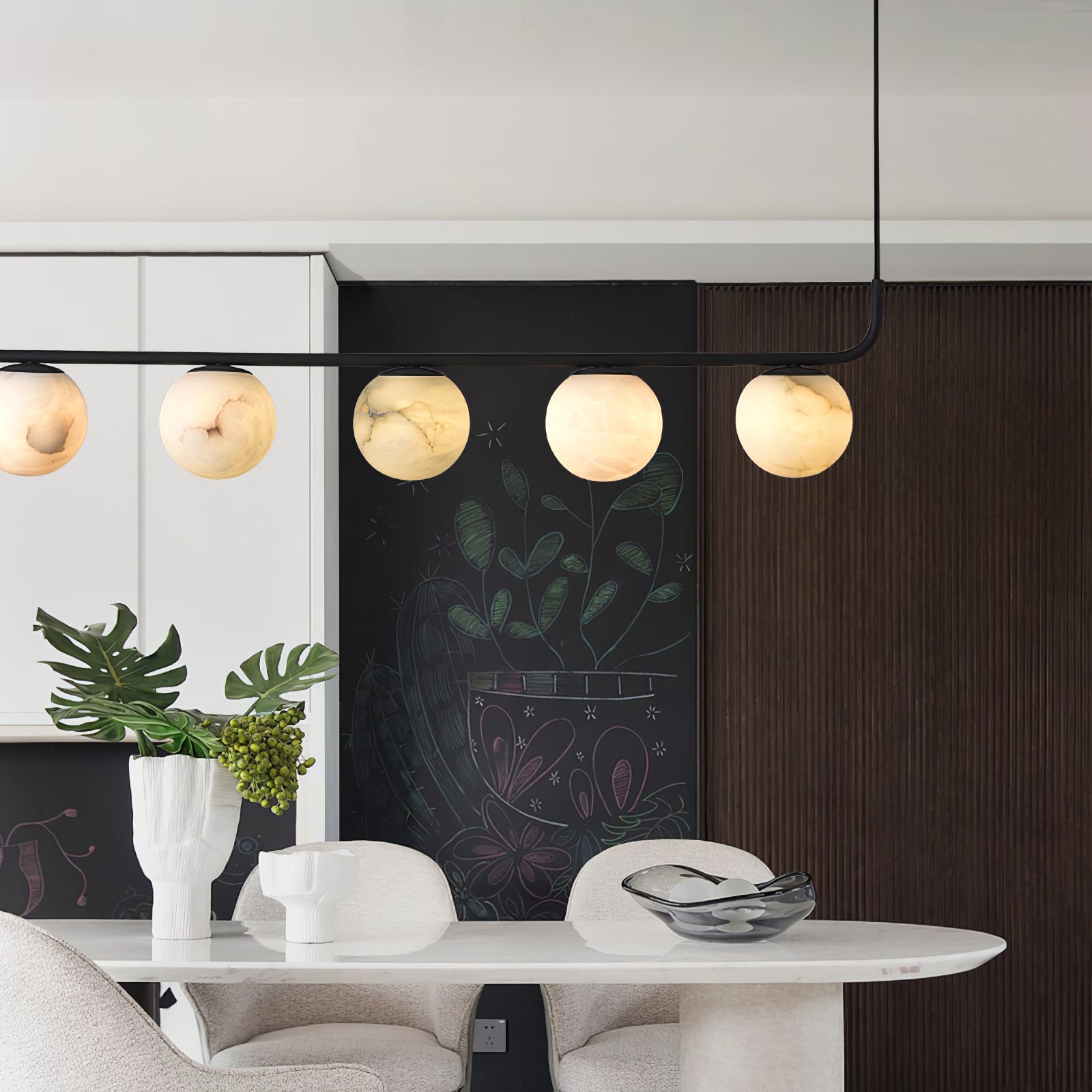 Five lit globes of the Clérachic pendant against a chalkboard wall and fluted dark timber, above an oval dining table.