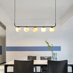 The Clérachic bar pendant hung high in a dining room, five alabaster globes reading warm against a white and blue wall.