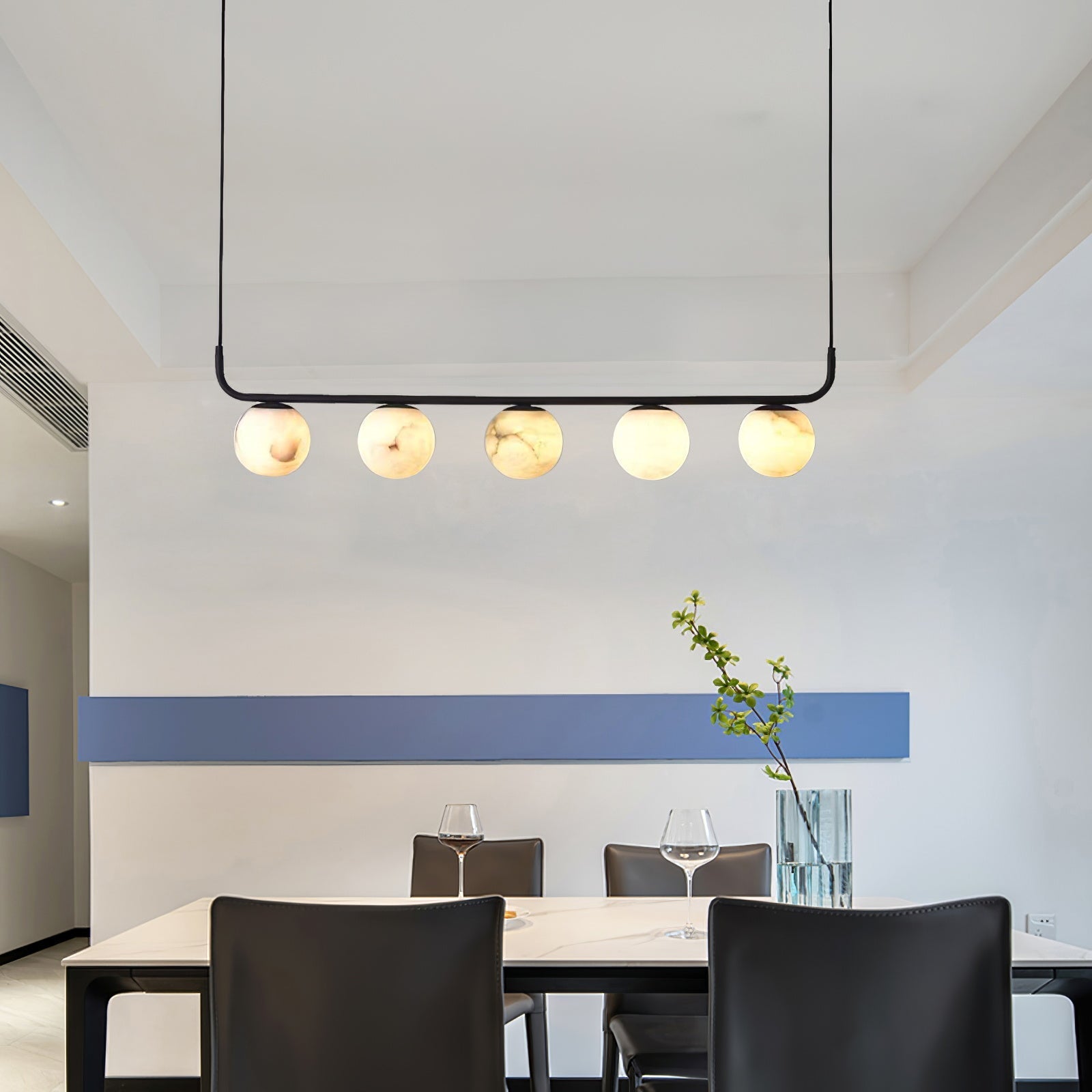 The Clérachic bar pendant hung high in a dining room, five alabaster globes reading warm against a white and blue wall.