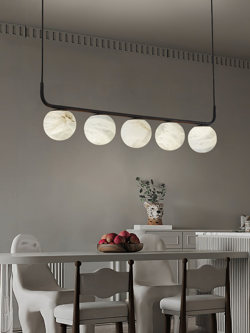 Clérachic bar pendant against a warm grey wall with dentil moulding, the globes lit softly above a long dining table.