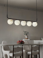 Clérachic bar pendant against a warm grey wall with dentil moulding, the globes lit softly above a long dining table.
