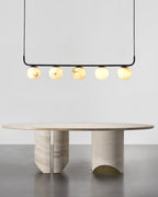 The Clérachic five-globe bar lit above an oval travertine table, each sphere showing its own veining.