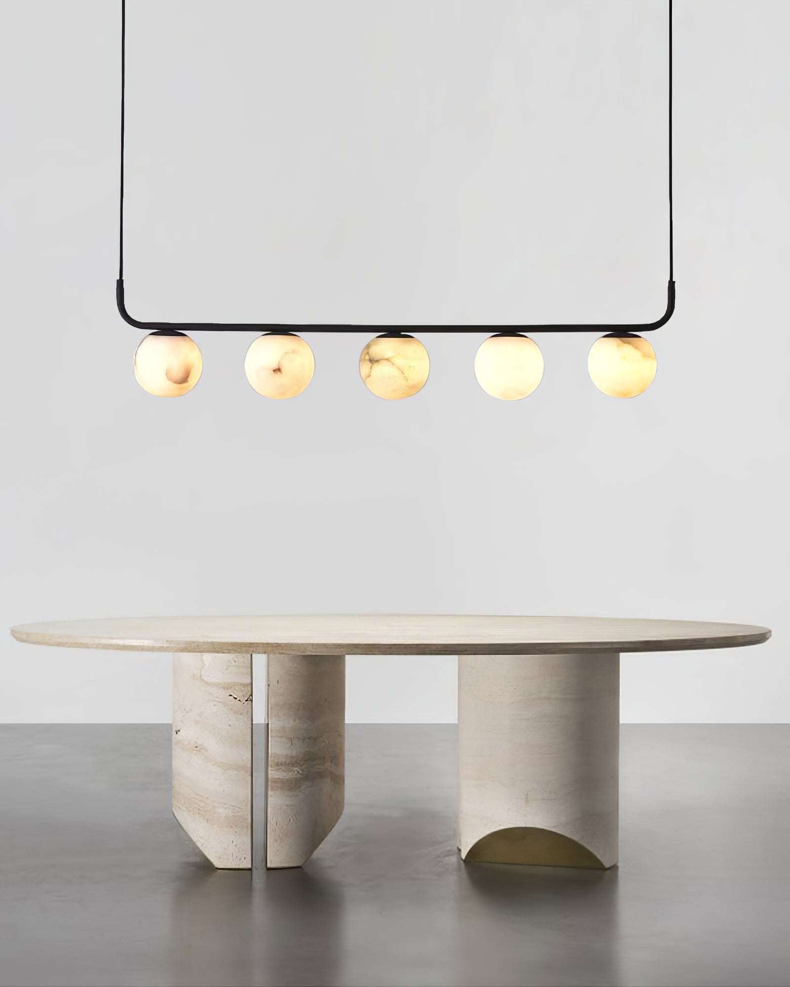 The Clérachic five-globe bar lit above an oval travertine table, each sphere showing its own veining.