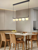 Clérachic bar pendant seen with its oval ceiling plate, five globes glowing over a marble table and tan leather chairs.