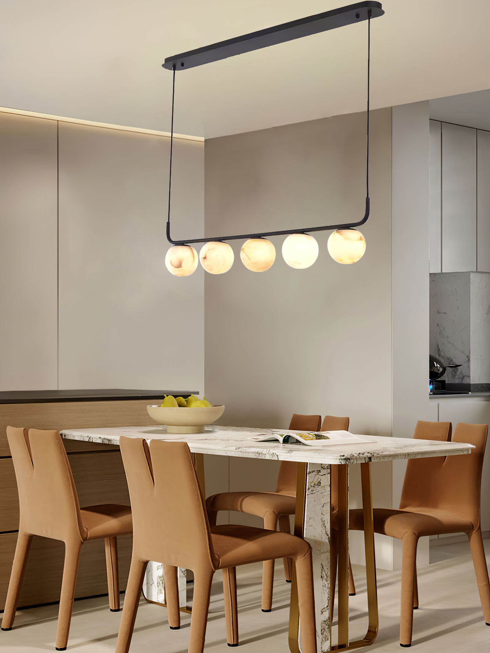 Clérachic bar pendant seen with its oval ceiling plate, five globes glowing over a marble table and tan leather chairs.