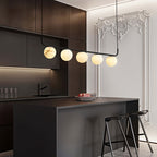 The Clérachic pendant lighting a dark kitchen island, five alabaster globes bright against ornate white wall moulding.