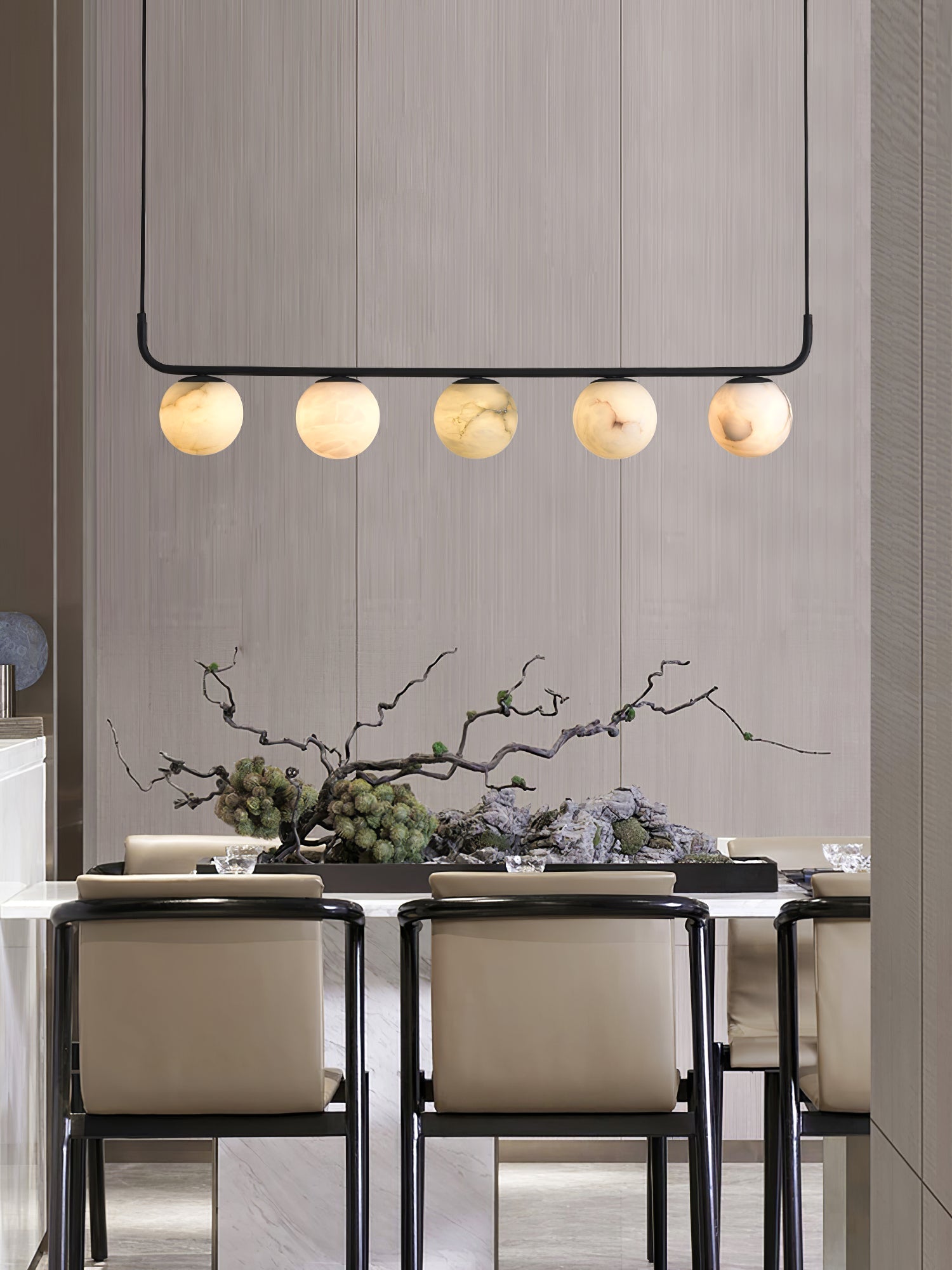 Clérachic five-globe bar over a marble dining table, warm light against a grasscloth wall and a sculptural branch display.