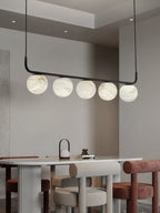 Clérachic pendant over a rounded dining table, five alabaster globes above ribbed pedestals and soft upholstered stools.