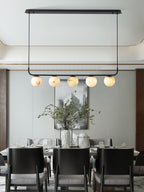 The Clérachic bar pendant with its oval plate, five globes lit above a dining table set for a formal meal.