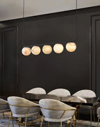 Clérachic five-globe bar glowing against a black panelled wall, above grey velvet chairs on brass frames.