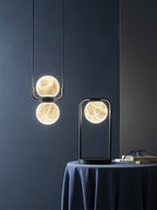 The Clérachic two-globe pendant against a deep blue wall, veining glowing through the stone beside a lit table lamp.
