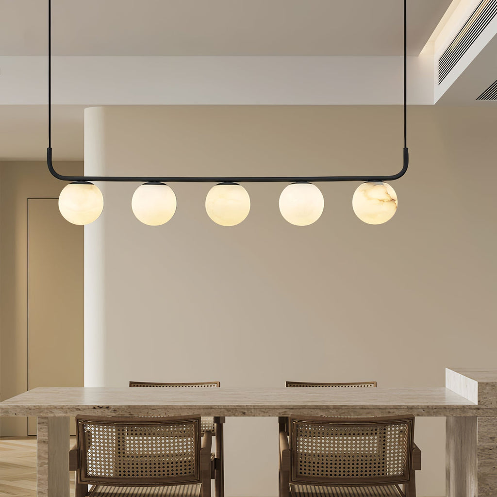 Clérachic five-globe bar above a stone dining table, warm light spilling across cane-backed chairs and cream walls.