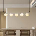 Clérachic five-globe bar above a stone dining table, warm light spilling across cane-backed chairs and cream walls.