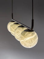 The Clérachic bar pendant seen in perspective, globes receding along the black rail with veining alight in each one.