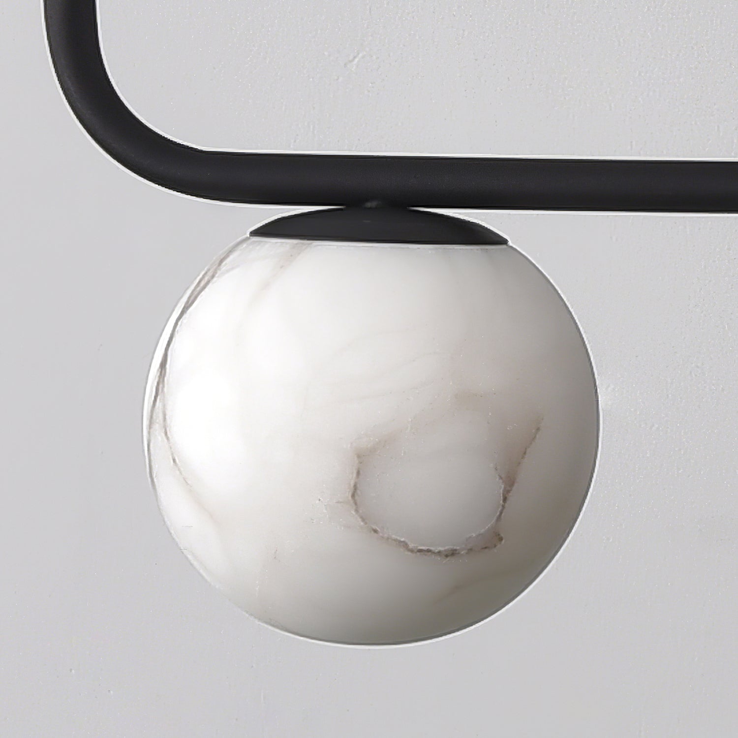 Close detail of one Clérachic alabaster globe seated under the matte-black bar, showing the fitting that holds it.