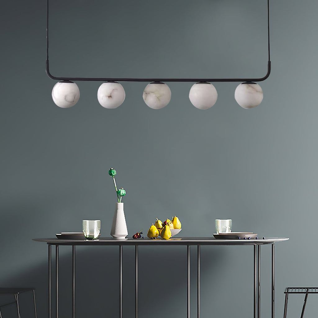 The Clérachic bar pendant against a teal-grey wall, five globes hovering above a slim console laid with fruit.