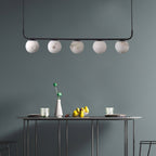 The Clérachic bar pendant against a teal-grey wall, five globes hovering above a slim console laid with fruit.