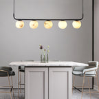 Clérachic five-globe pendant over a marble-topped island, warm globes lit above brass-legged bar stools.