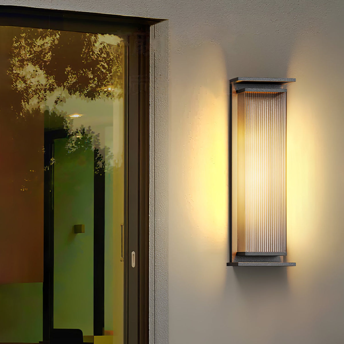 A Clérachic wall light on a rendered wall beside a tall glazed door, lit warm, with trees reflected in the glass.