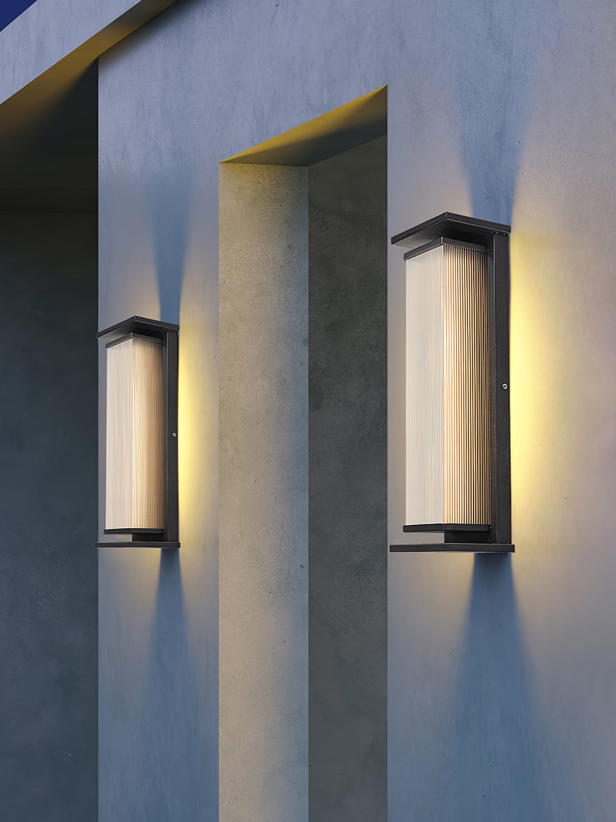 Two Clérachic wall lights flank a concrete-grey recess on an outer wall, both shining warm light up and down.