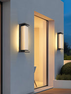 Two Clérachic wall lights, one tall and one short, on a pale outside wall by a sliding glass door that opens onto a timber deck.