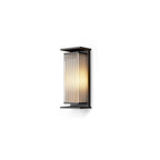 A short Clérachic wall light with a ribbed shade glowing white, in a black frame on a plain white backdrop.