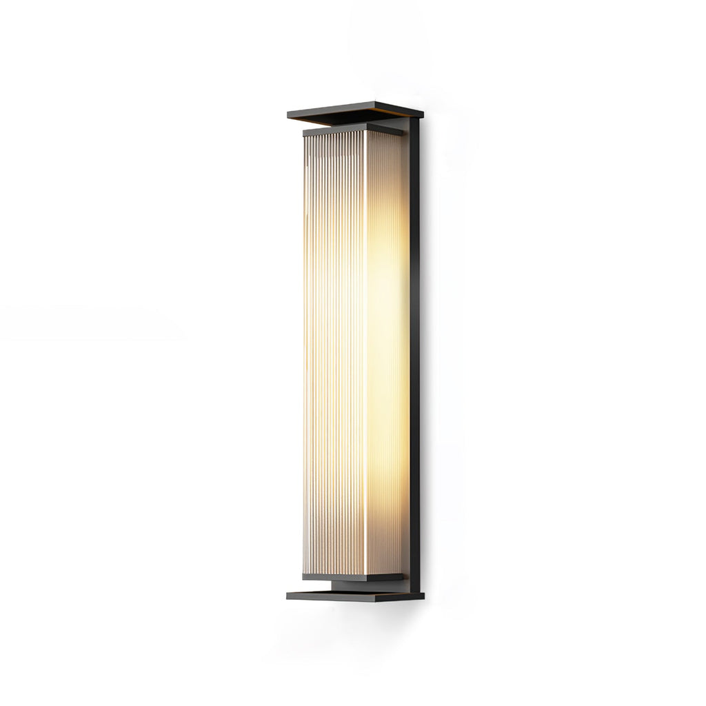 A tall Clérachic wall light with a ribbed shade lit warm, on a plain white backdrop and a soft shadow.