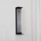 A Clérachic wall light unlit, angled slightly to show the black shelf at its base and the fine ribs in the glass.
