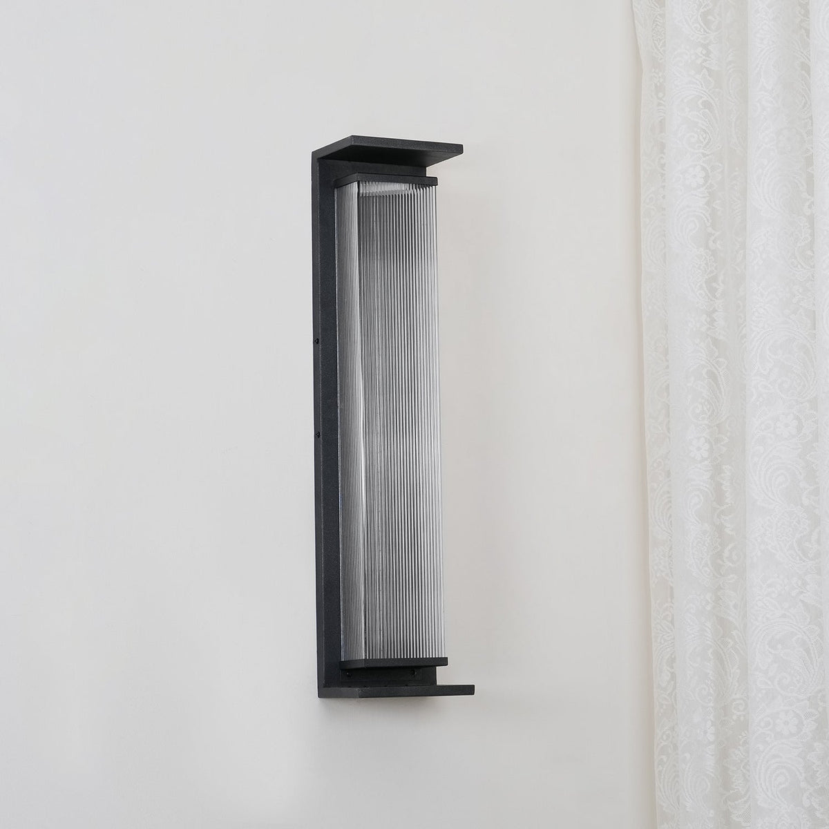 A Clérachic wall light unlit, angled slightly to show the black shelf at its base and the fine ribs in the glass.
