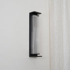 A Clérachic wall light unlit and viewed from the side, with a clear ribbed shade inside a slim black frame.