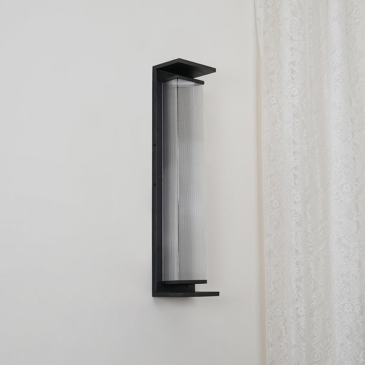 A Clérachic wall light unlit and viewed from the side, with a clear ribbed shade inside a slim black frame.