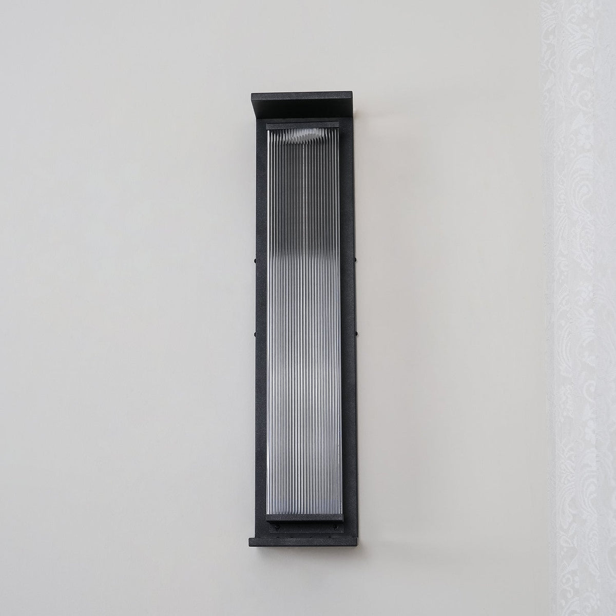 A Clérachic wall light unlit on a plain pale wall, with a black frame around clear ribbed glass.