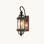 A Clérachic outdoor wall lantern with a black curved arm, clear glass panels and a small pointed finial, on a plain white backdrop.