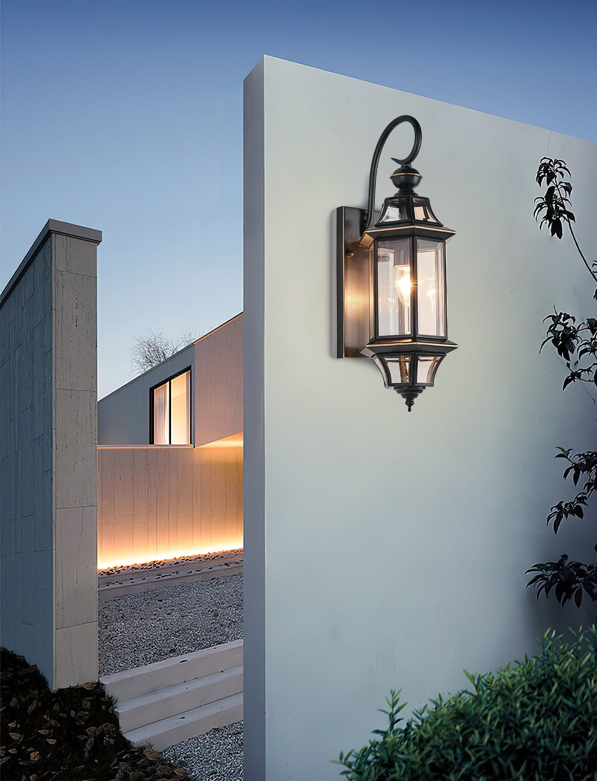A Clérachic wall lantern on a pale rendered wall of a modern house, under a clear blue evening sky.