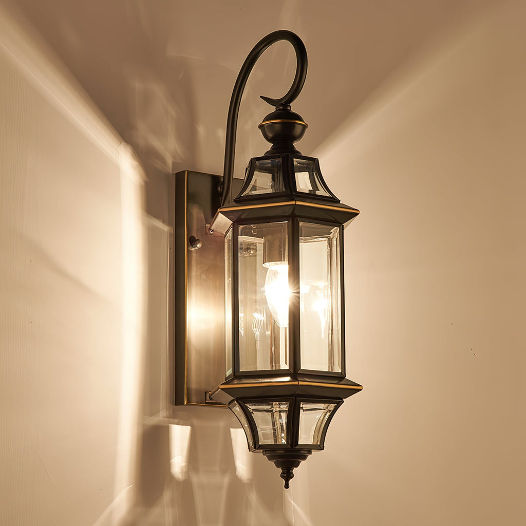 A Clérachic wall lantern lit against a warm cream wall, throwing light and shadow from its glass panels.