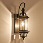 A Clérachic wall lantern lit against a warm cream wall, throwing light and shadow from its glass panels.