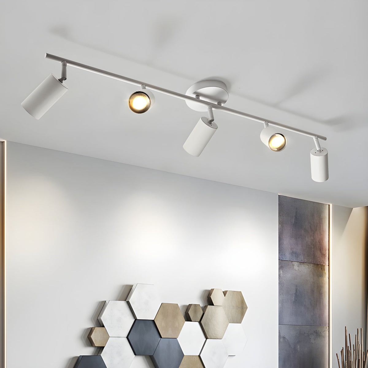 Angled view of a white Clérachic five-head track light above a wall with a hexagon tile display, the bulbs glowing.