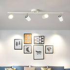 A white Clérachic four-head track light on a grey ceiling lights a gallery of framed prints above a sofa.