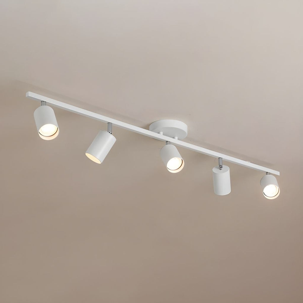 A white Clérachic five-head track light seen from below against a warm taupe ceiling, each head angled a different way.
