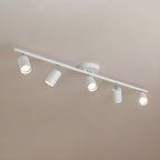 A white Clérachic five-head track light seen from below against a warm taupe ceiling, each head angled a different way.